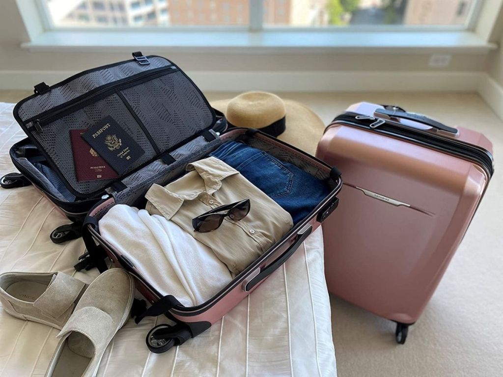 rose colored luggage opened on bed with clothing inside