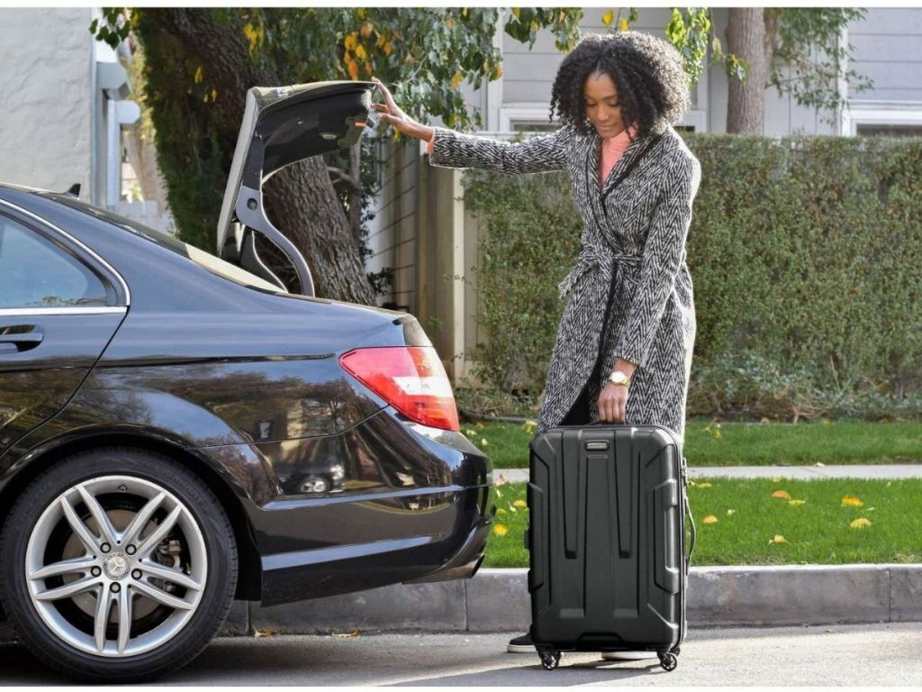 woman putting black luggage into car trunk
