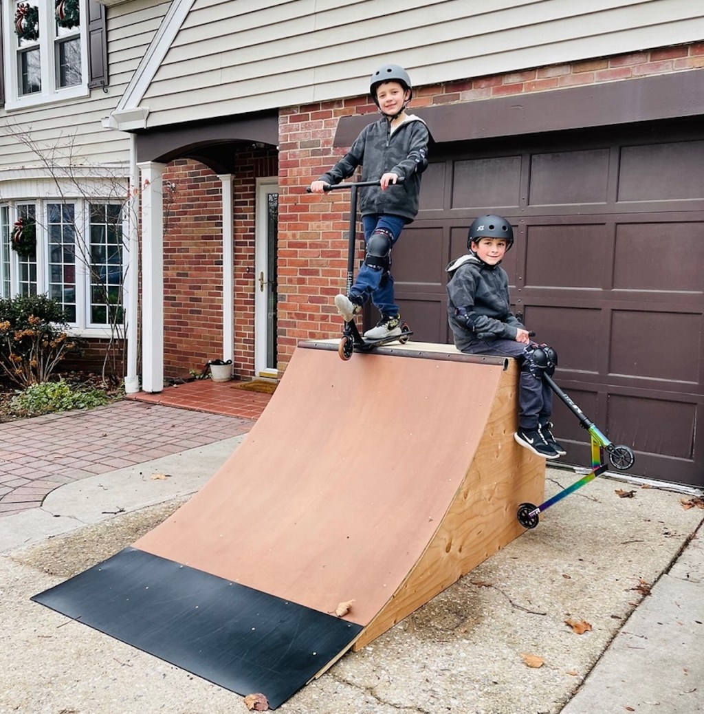 boys with scooters on top of wooden skateboard ramp