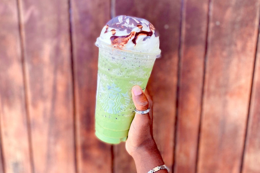 hand holding a green starbucks frappuccino halloween drink in front of wood wall