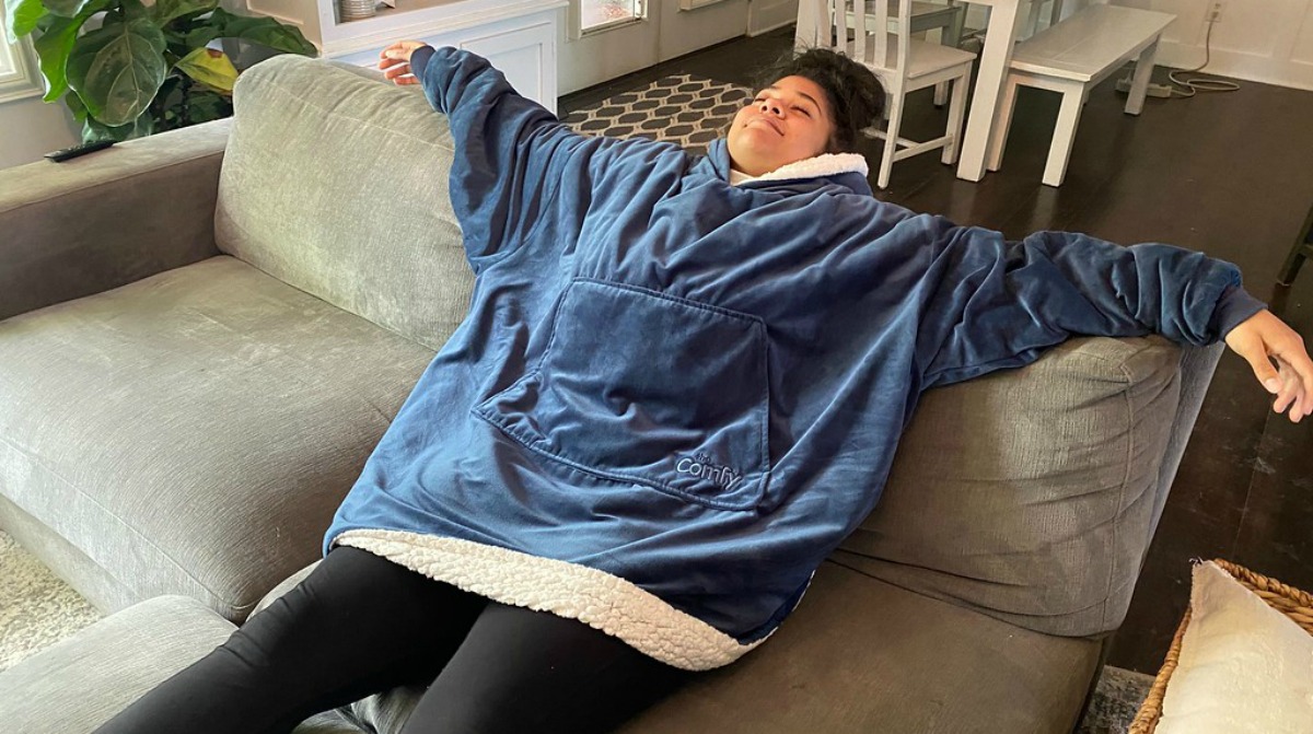 girl lounging on couch wearing a comfy jr blanket