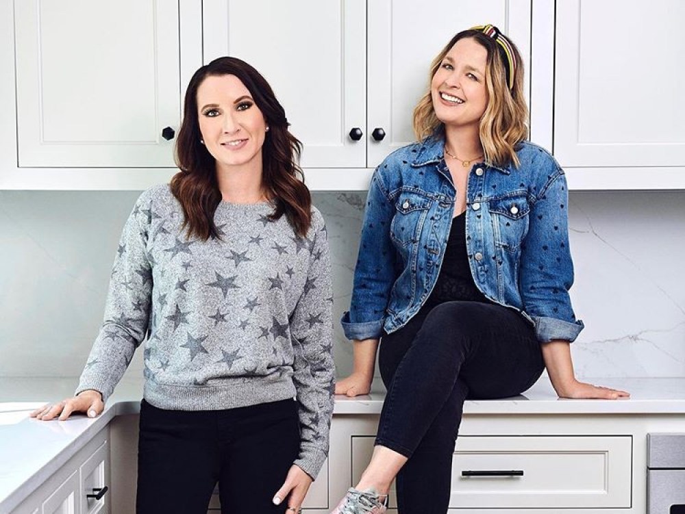 stars of The Home Edit in kitchen, one sitting on counter, one standing next to her