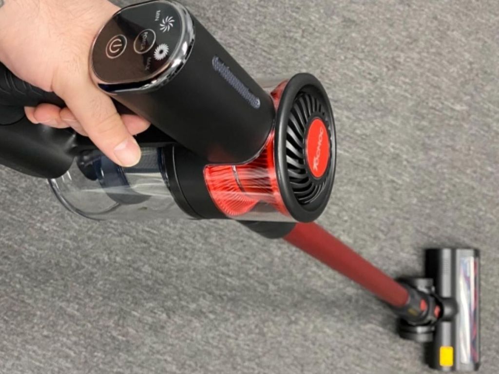 hand holding red and black stick vacuum cleaning a gray carpet