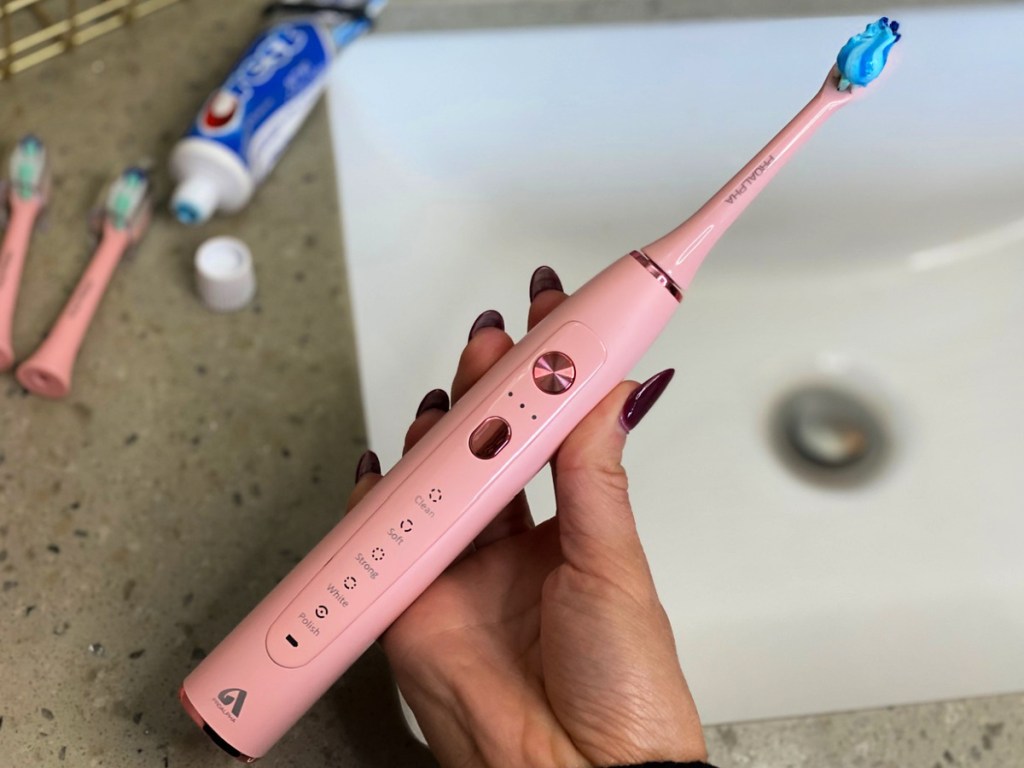 woman holding a ProAlpha Sonic Electric Toothbrush in pink