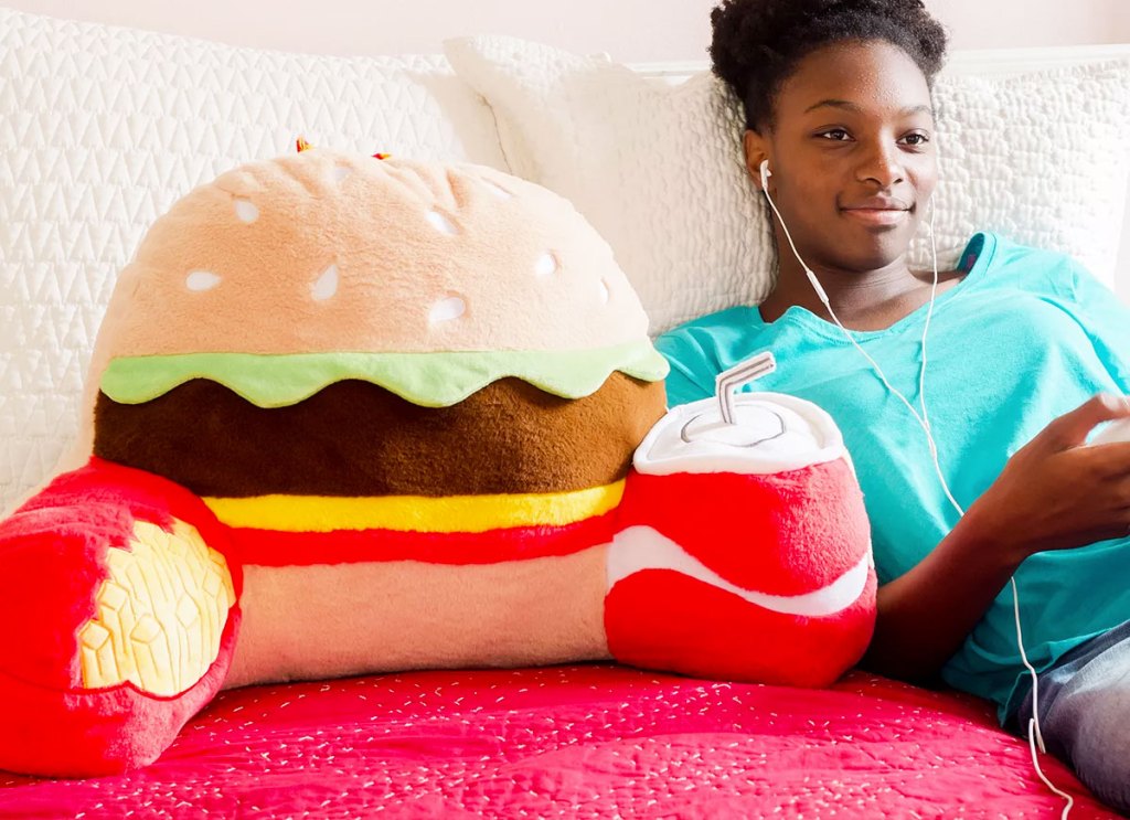 boy laying on bed listening to mustic next to a hamburger shaped backrest pillow