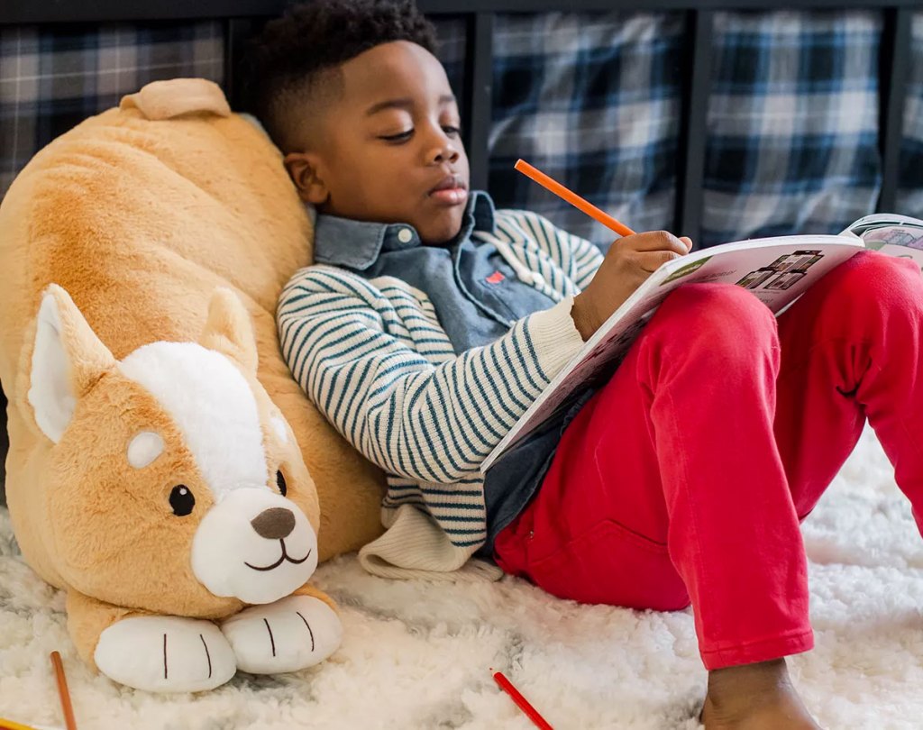 boy coloring in a coloring book and leaning against a corgi shaped backrest pillow
