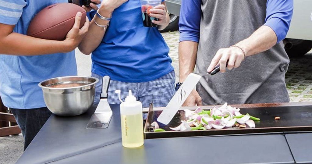 three people standing in front of flat top griddle with one of them using spatula to took vegetables