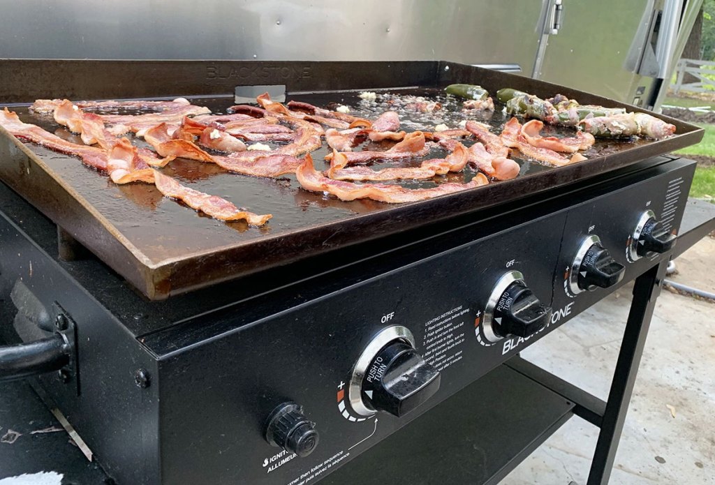 black blackstone griddle in backyard with strips of bacon cooking on it