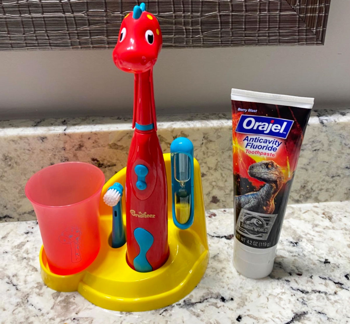 red dinosaur themed kids electric toothbrush set with timer and rinse cup on a bathroom counter