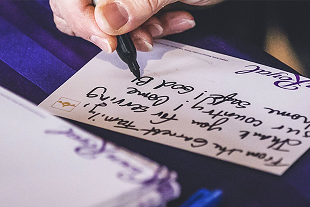 person using a black sharpie marker to write a note to include in a crown royal care package