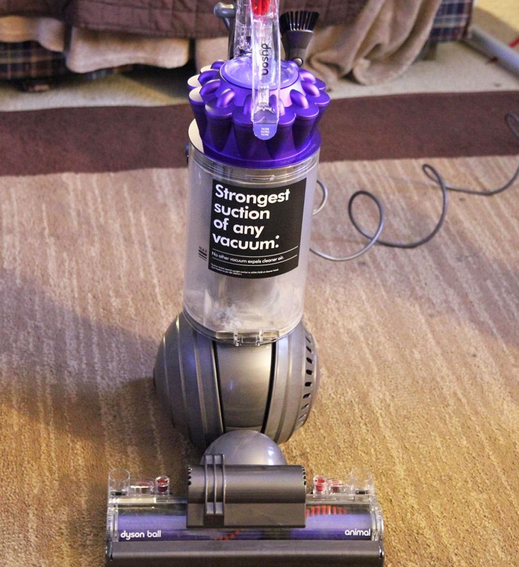 grey and purple dyson upright vacuum on a beige area rug