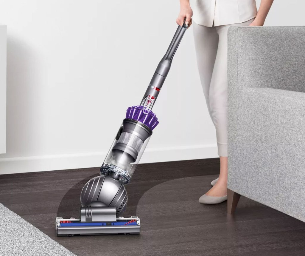 woman using a dyson ball upright vacuum to clean up dust around a couch