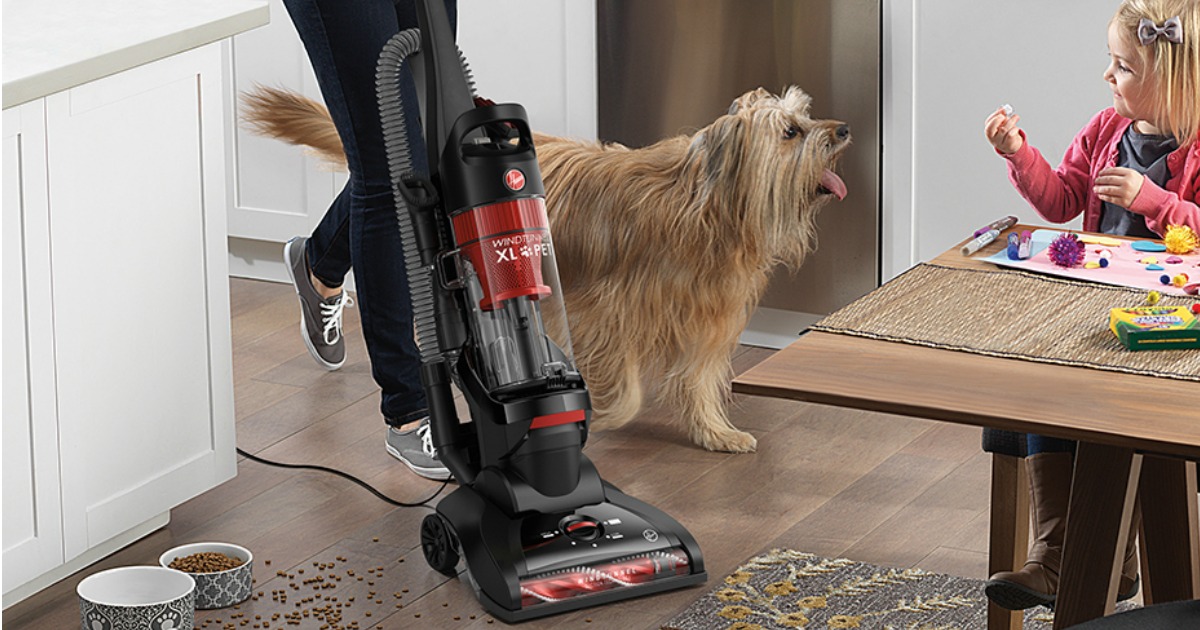 Woman using an upright vacuum in the kitchen near a dog