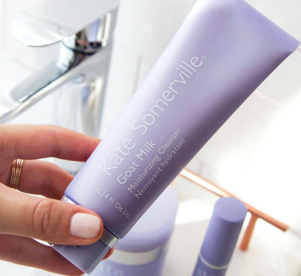 woman with light pink nails holding up a lilac colored tube of Kate Somerville cleanser