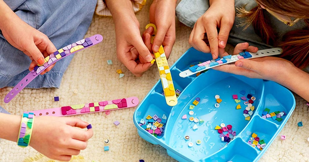 kids sitting on floor decorating lego dots bracelets with pieces inside a blue storage case