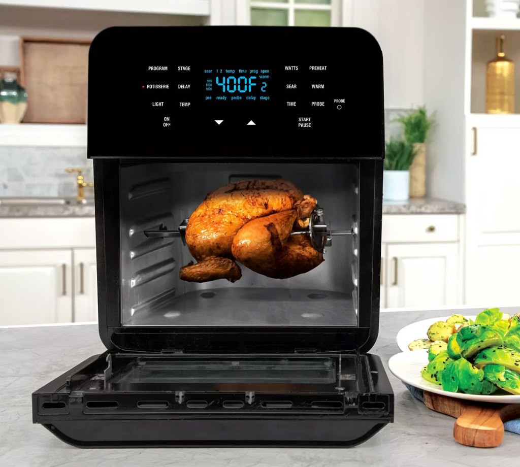 large black nuwave air fryer oven on counter with door open showing rotisserie chicken inside