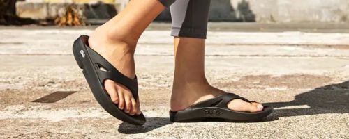 person walking in oofos sandals on concrete