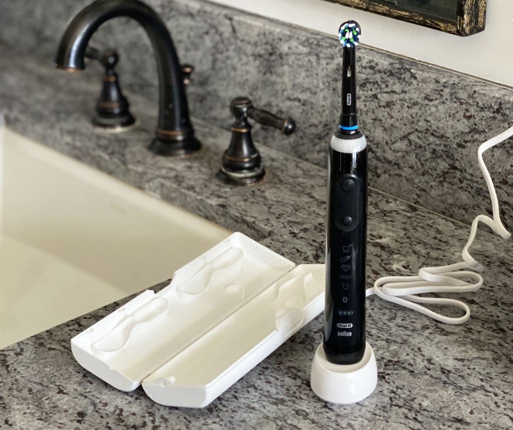 black oral-b electric toothbrush on bathroom counter on it's charging base next to a white travel case
