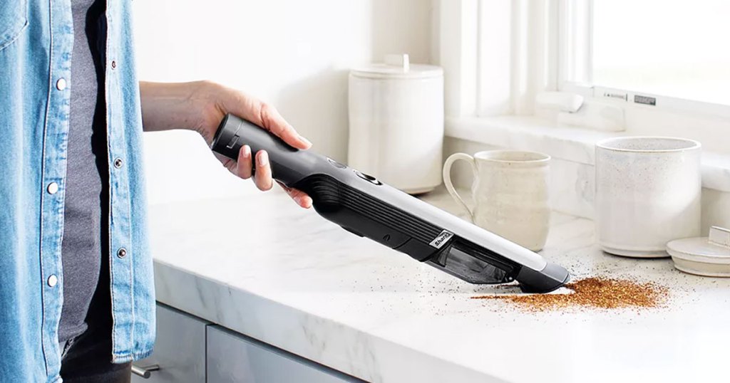 woman using a mini shark handheld vacuum to clean up coffee ground on kitchen counter