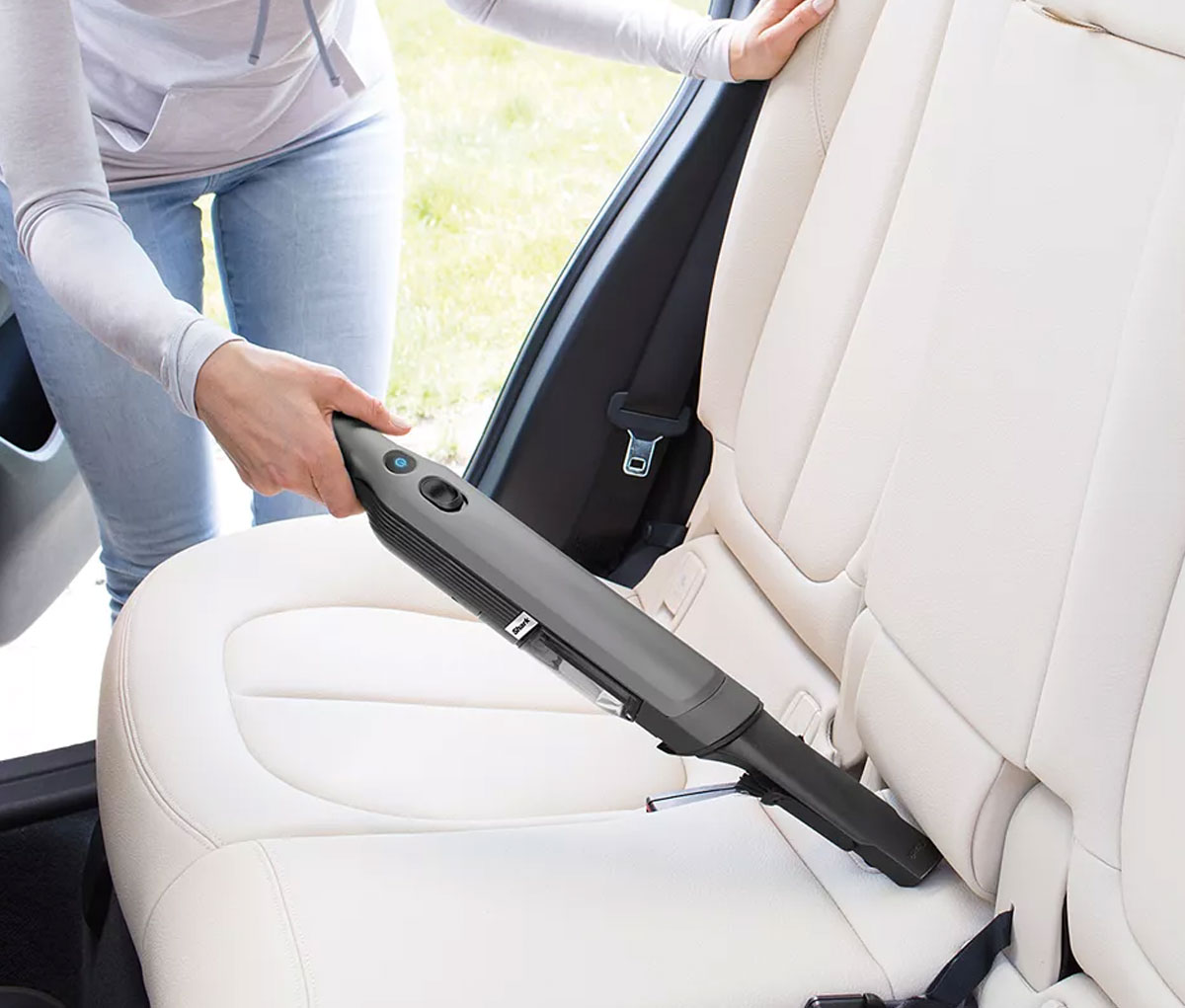 woman using a mini shark cordless vacuum to clean seats inside a car