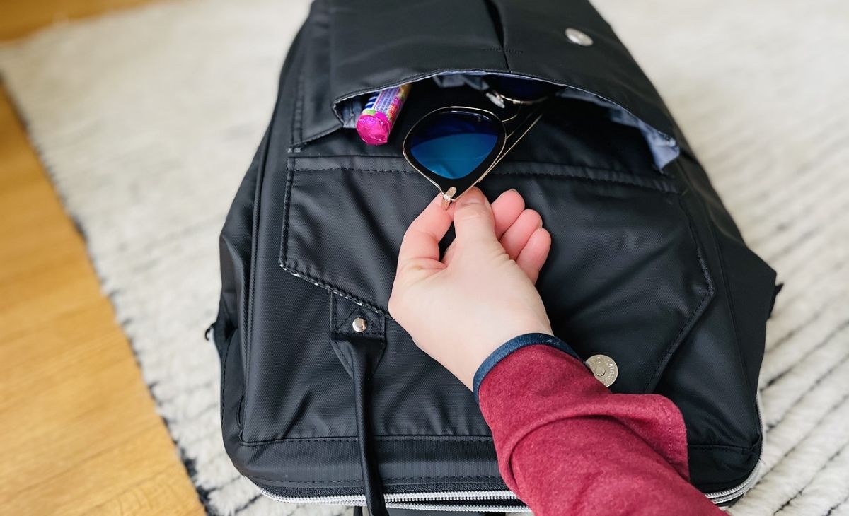 A hand placing some sunglasses in a backpack