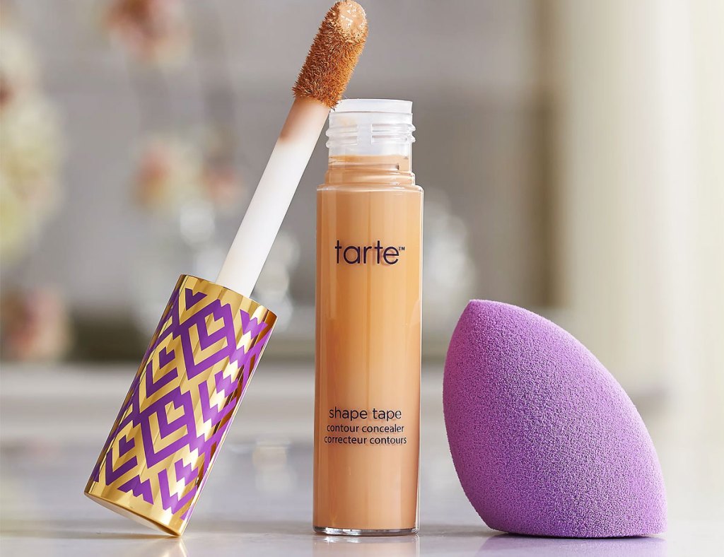 bottle of tarte spade tape with wand leaning against it and purple blending sponge