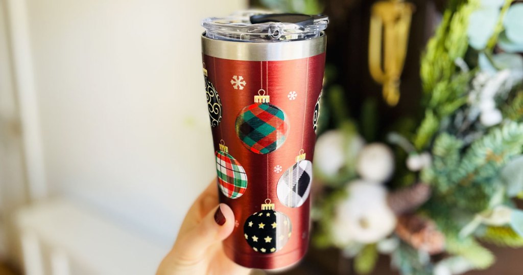 woman holding up red christmas themed tumbler with wreath in background