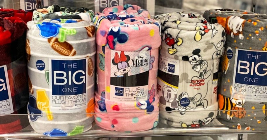 the big one throw blankets in football, mickey, and minnie mouse prints on a store display shelf