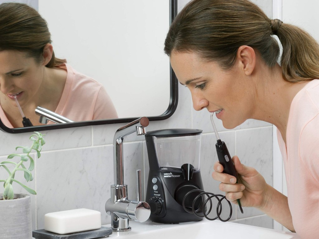 woman bending over a bathroom sink flossing her teeth with a waterpik