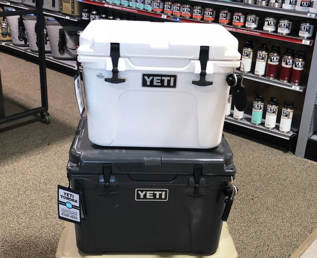 a smaller white yeti cooler stacked on top of a black one with shelves of yeti products in the background