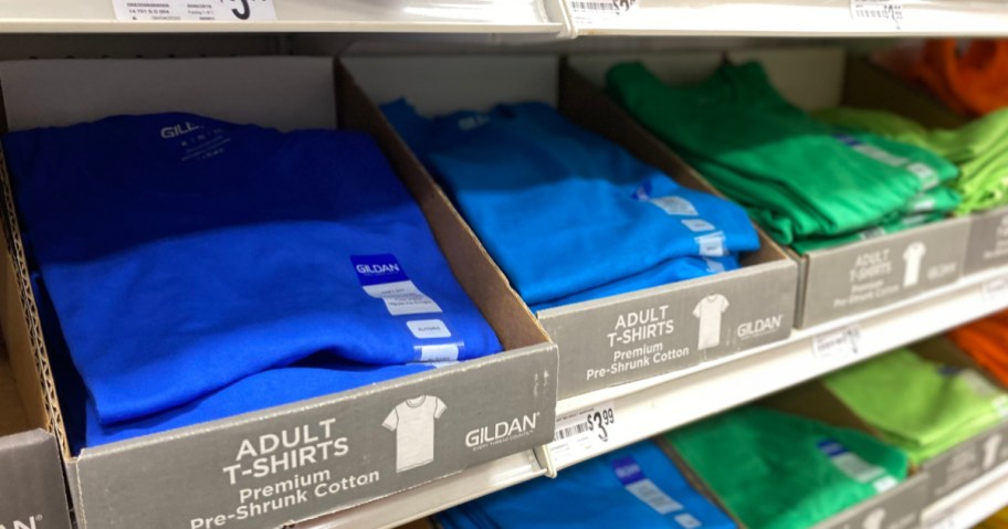 blue and green folded Gildan Shirts in boxes on shelf
