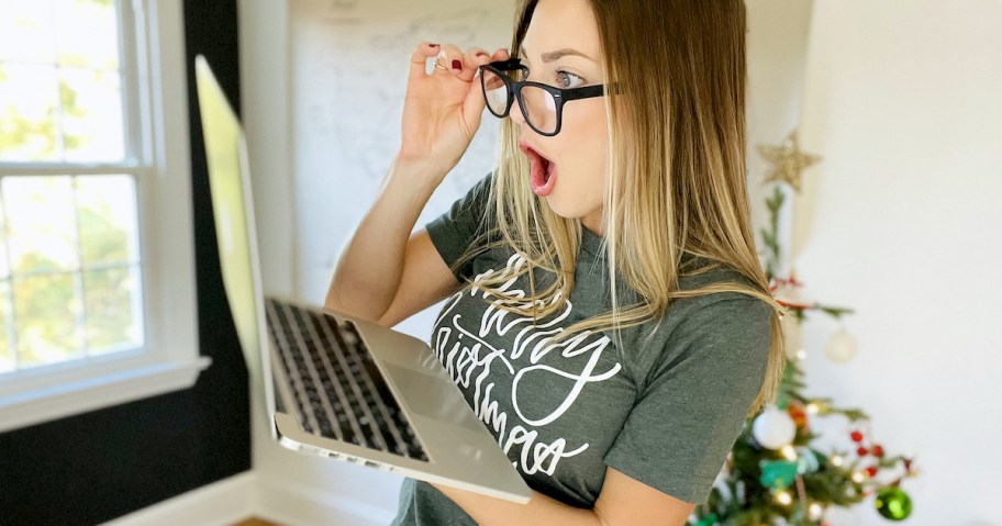 woman holding laptop while pulling down glasses acting surprised