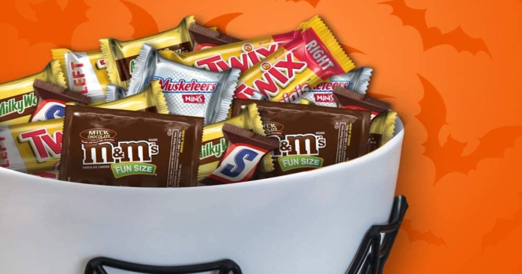 white bowl filled with mars fun size halloween candies. there is an orange background with darker orange shaped bats.