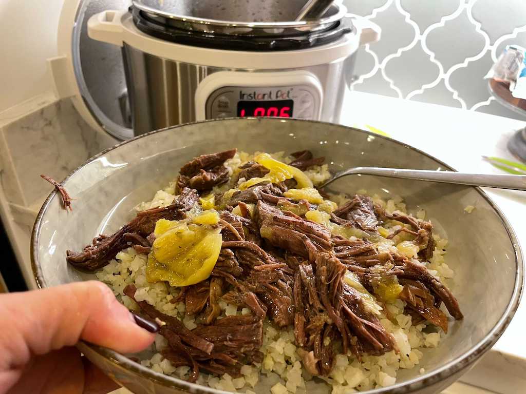 holding bowl plate with shredded beef and Instant Pot in the background
