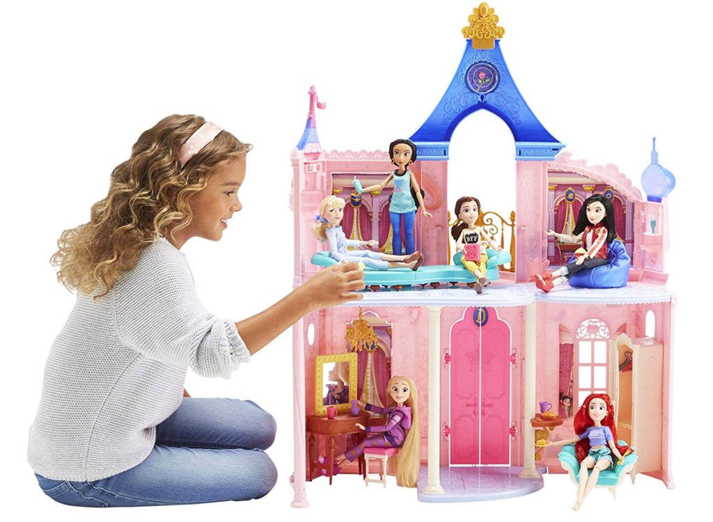 girl in white sweater and jeans playing with a pink disney princess castle playhouse