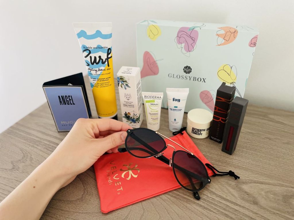 hand holding a pair of sunglasses by beauty products