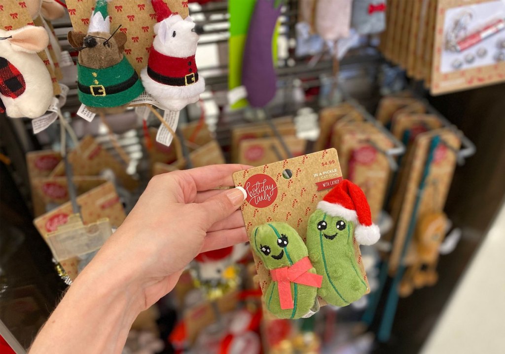 woman holding up a set of christmas pickle themed cat toys with more christmas toys in background