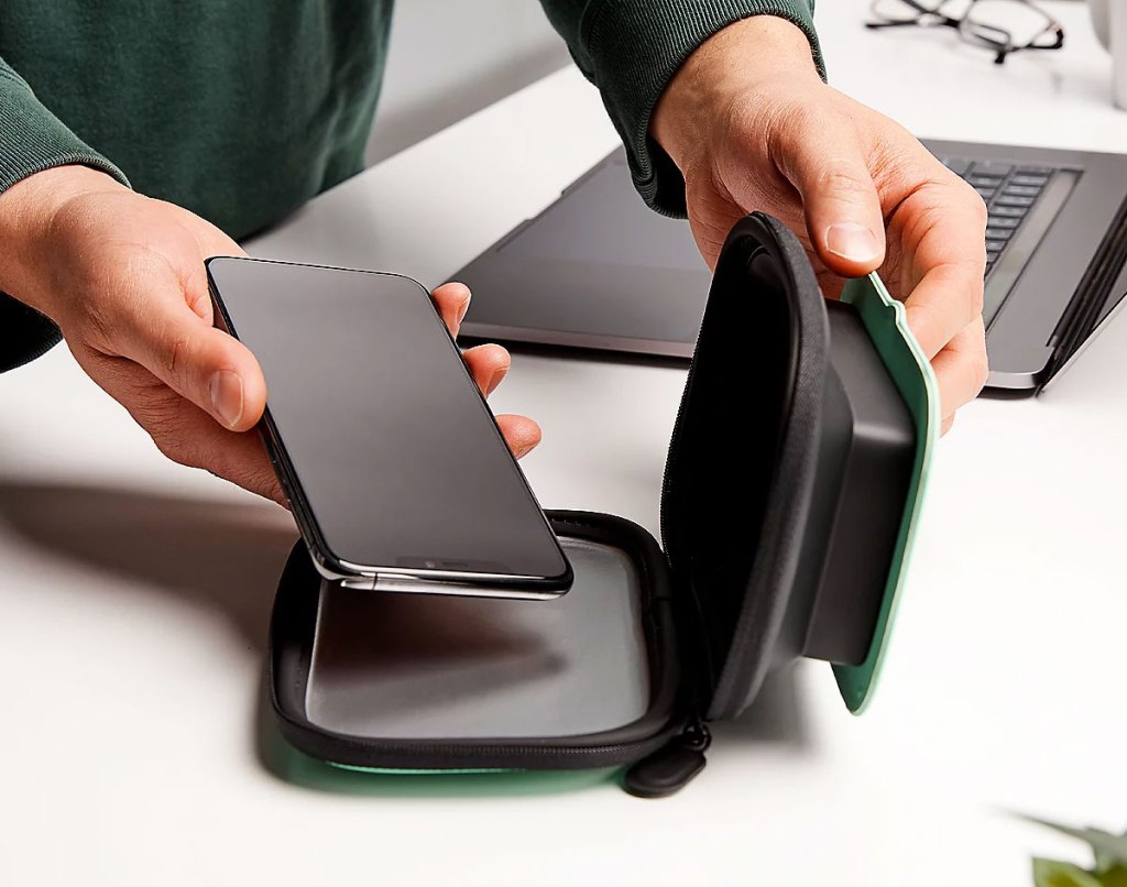 person placing a black smartphone into a black sanitizing case