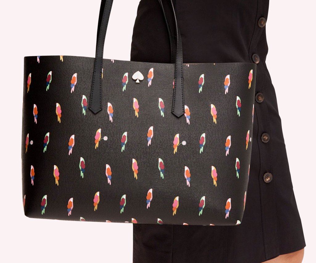 woman in black button-up skirt with a black kate spade tote bag on her arm that's covered in a parrot print