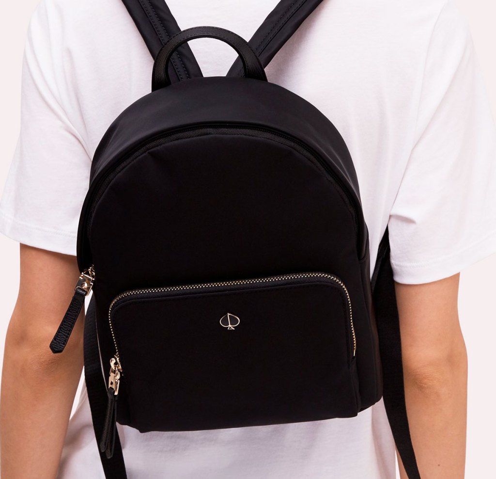 person in a white t-shirt with a small black kate spade backpack on their back