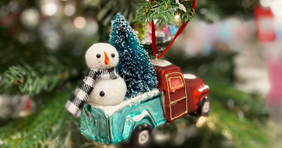 green and red truck ornament with christmas tree and snowman in back hanging on a christmas tree