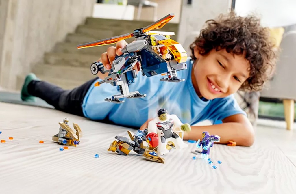 boy laying on floor holding up a lego avengers helicopter toy in the air