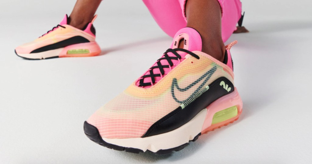 woman sitting down wearing a pink outfit and pink/peach nike max 2090 shoes