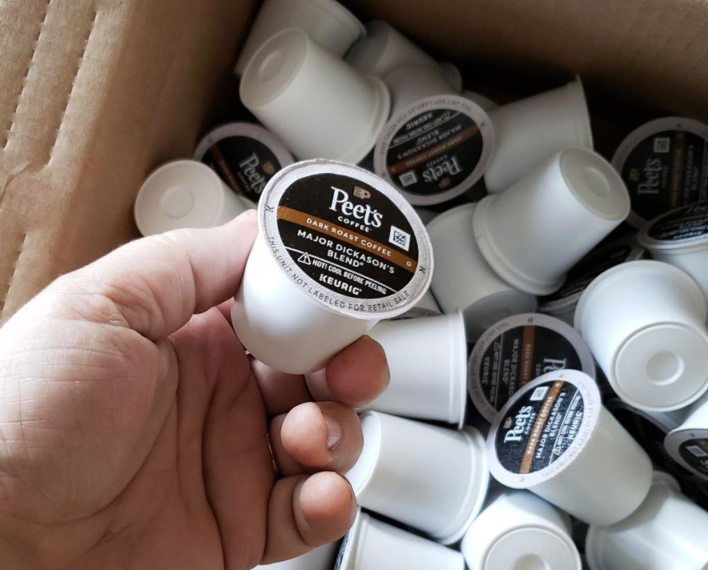 person holding up a peets k-cup with a large box full of k-cups in the background
