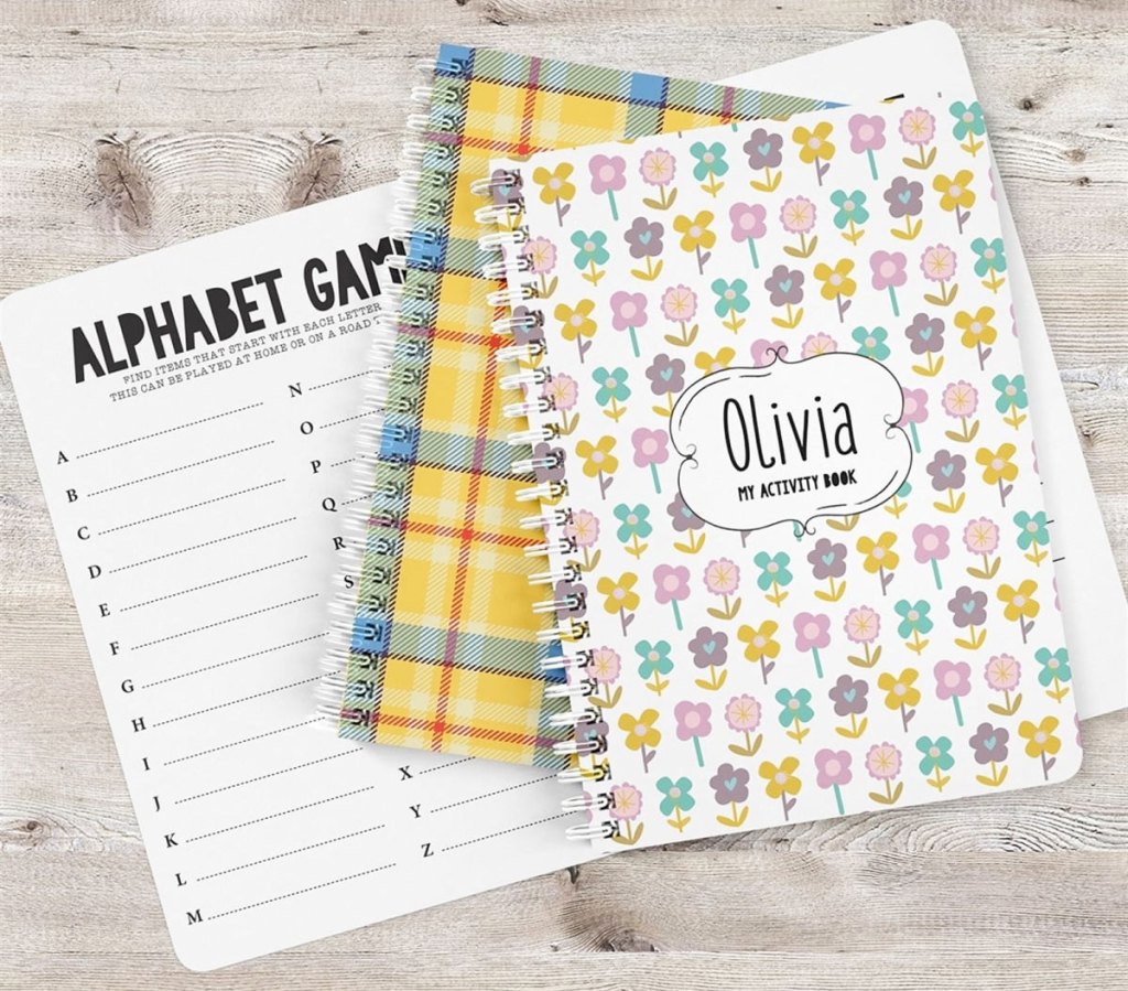 two spiral bound printed notebooks with personalized names on them with an alphabet games activity sheet beneath them