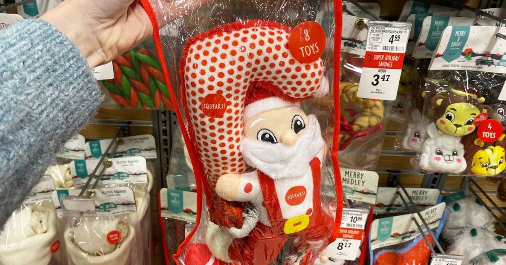 woman in a grey sweater holding up a plastic stocking filled with christmas theme dog toys