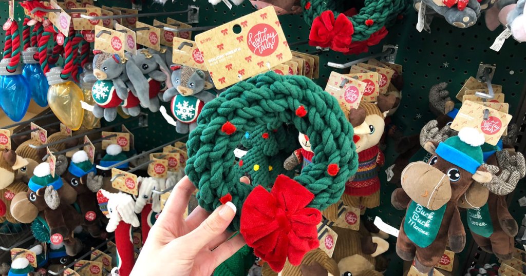 woman holding up a christmas wreath shaped rope dog toy with more christmas toys in background