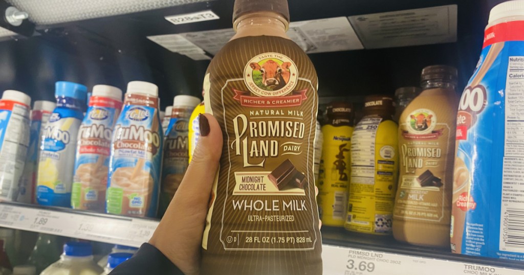 hand holding bottle of chocolate milk in front of store refrigerator