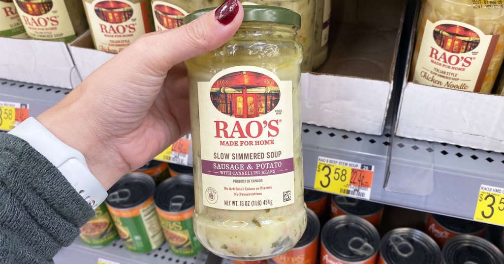 woman holding up a jar of rao's soup in front of walmart shelf of more jarred soups