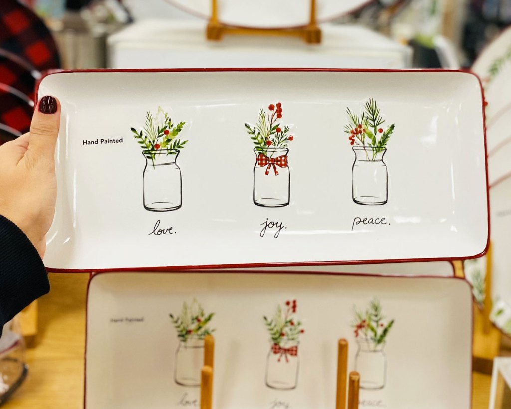 woman holding up a white rectangular thin platter that say love joy peace with mason jars full of christmas tree branches